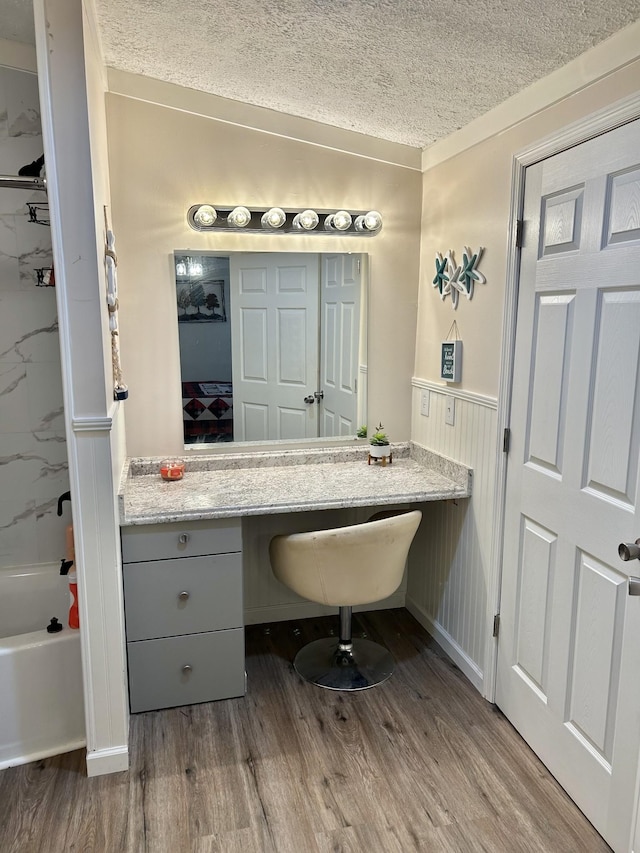 full bathroom featuring a wainscoted wall, a textured ceiling, and wood finished floors