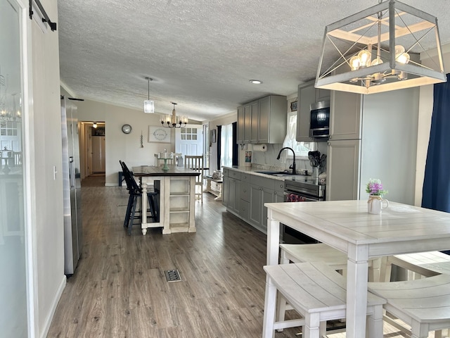 kitchen with dark wood-style flooring, a notable chandelier, gray cabinets, a barn door, and a sink