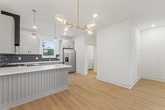 kitchen with stainless steel appliances, decorative light fixtures, kitchen peninsula, white cabinets, and light hardwood / wood-style floors