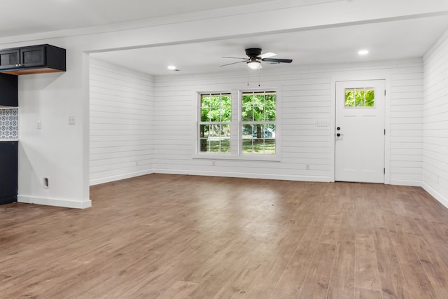 unfurnished living room with ceiling fan, wooden walls, and hardwood / wood-style floors