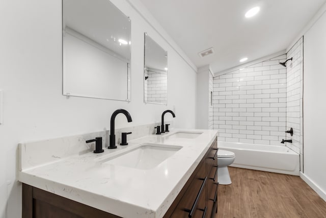 full bathroom featuring hardwood / wood-style flooring, vaulted ceiling, tiled shower / bath combo, vanity, and toilet