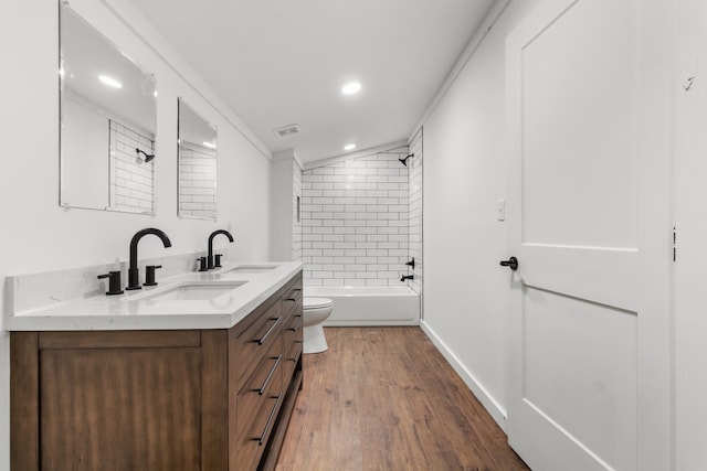 full bathroom with tiled shower / bath, vanity, hardwood / wood-style flooring, crown molding, and toilet