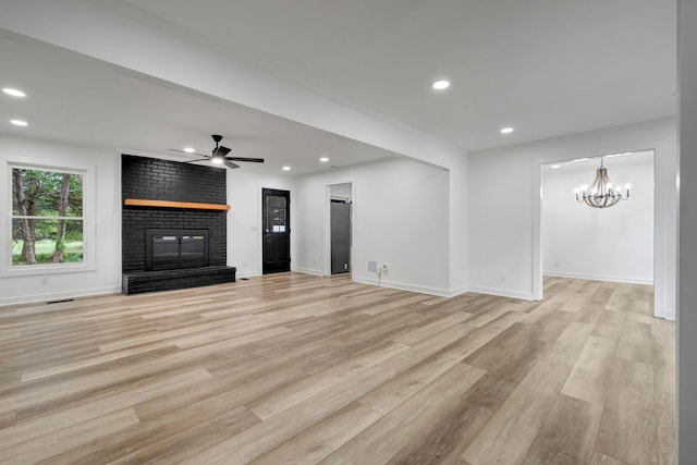 unfurnished living room with a fireplace, ceiling fan with notable chandelier, and light hardwood / wood-style flooring