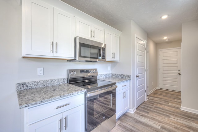 kitchen featuring appliances with stainless steel finishes, white cabinetry, light stone counters, light hardwood / wood-style floors, and a textured ceiling