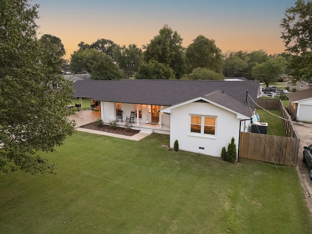 back house at dusk featuring a lawn