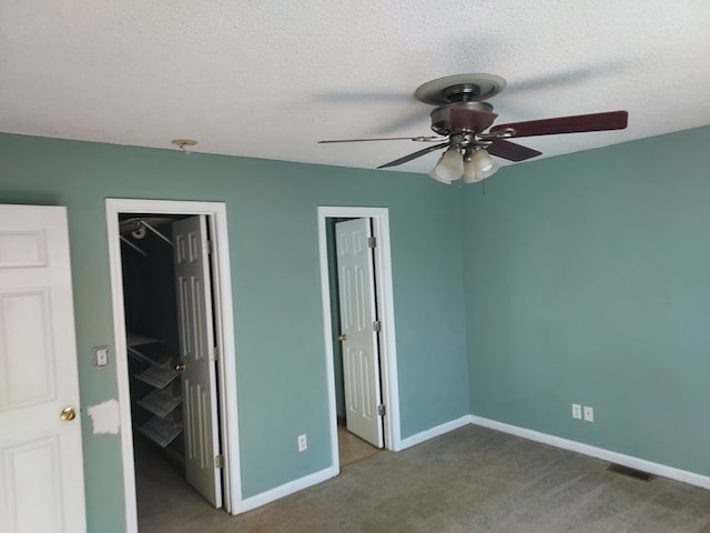 unfurnished bedroom featuring ceiling fan, a spacious closet, a textured ceiling, a closet, and carpet