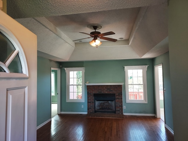 unfurnished living room with a textured ceiling, a raised ceiling, ceiling fan, a fireplace, and dark hardwood / wood-style floors