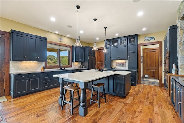 kitchen with light hardwood / wood-style flooring, appliances with stainless steel finishes, an island with sink, a kitchen bar, and decorative backsplash