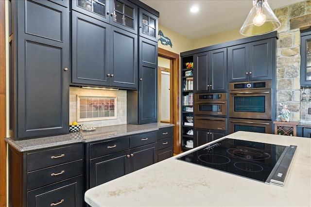 kitchen with black electric stovetop, backsplash, decorative light fixtures, light stone counters, and double oven