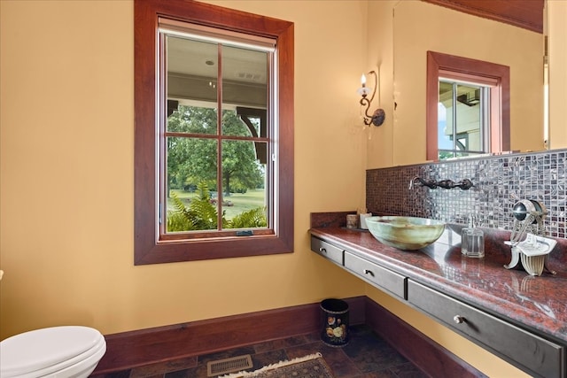 bathroom featuring vanity, toilet, a healthy amount of sunlight, and backsplash