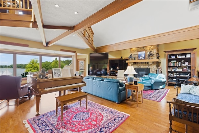 living room with a textured ceiling, a stone fireplace, hardwood / wood-style flooring, and lofted ceiling with beams