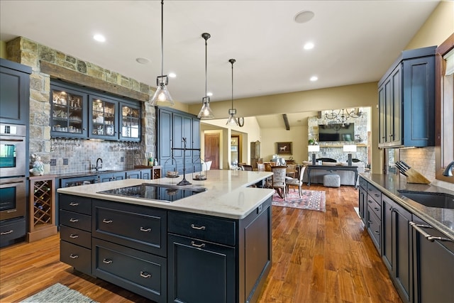 kitchen with hanging light fixtures, hardwood / wood-style flooring, sink, a stone fireplace, and a center island with sink