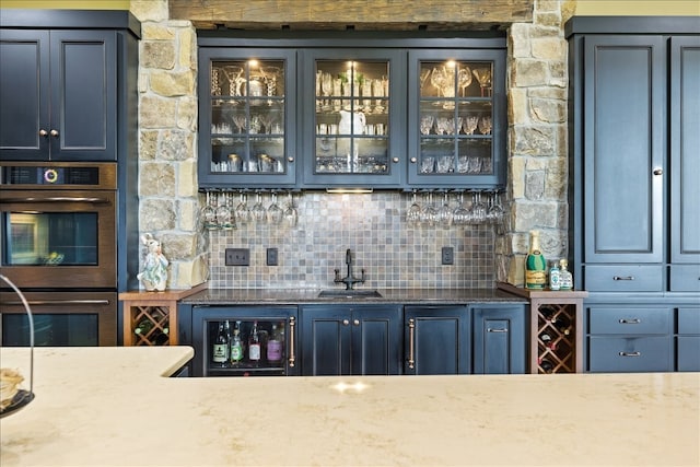 bar featuring blue cabinets, decorative backsplash, stainless steel double oven, and sink