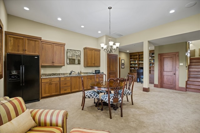 kitchen with light stone counters, a notable chandelier, light carpet, black fridge, and pendant lighting