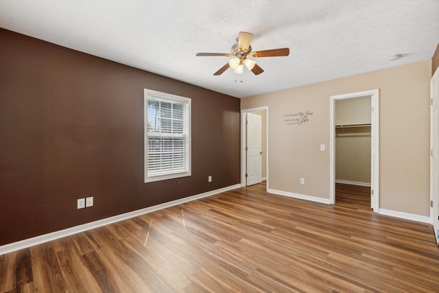 unfurnished bedroom featuring hardwood / wood-style flooring, a walk in closet, a closet, ceiling fan, and a textured ceiling