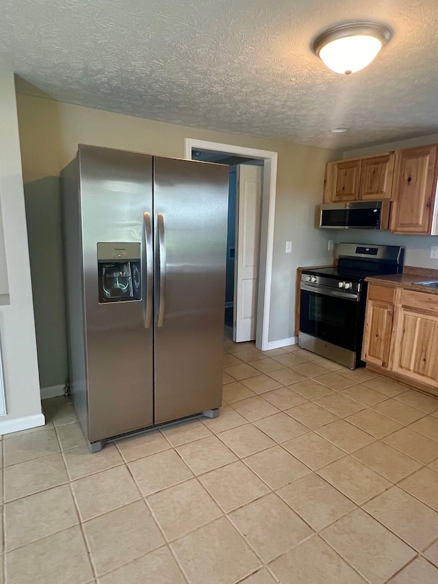 kitchen with appliances with stainless steel finishes, a textured ceiling, and light tile patterned flooring