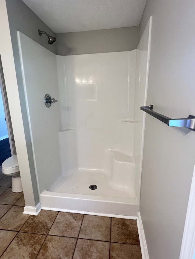 bathroom featuring toilet, a shower, and a textured ceiling