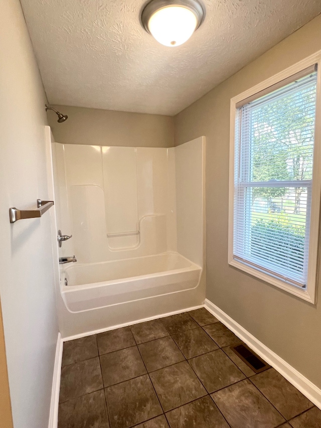 bathroom featuring tile patterned flooring, bathtub / shower combination, and a textured ceiling