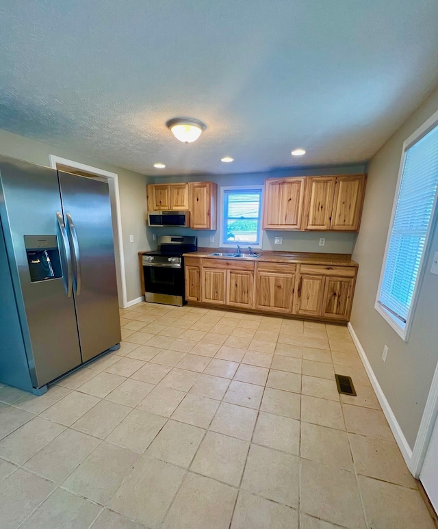 kitchen featuring a textured ceiling, sink, appliances with stainless steel finishes, and light tile patterned flooring