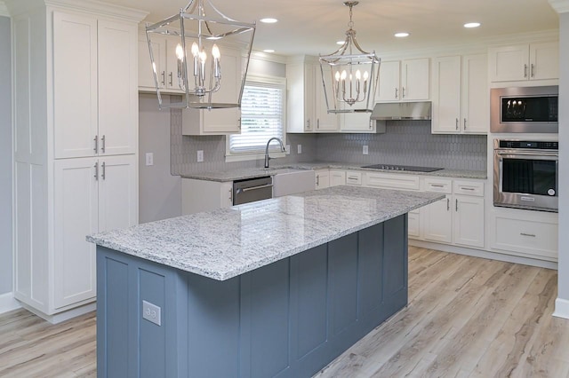 kitchen with under cabinet range hood, a chandelier, appliances with stainless steel finishes, light wood-style floors, and white cabinetry