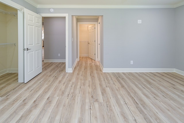 unfurnished bedroom featuring ornamental molding, a walk in closet, a closet, and light hardwood / wood-style floors