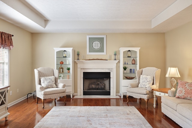 sitting room featuring a premium fireplace, dark hardwood / wood-style floors, and a raised ceiling