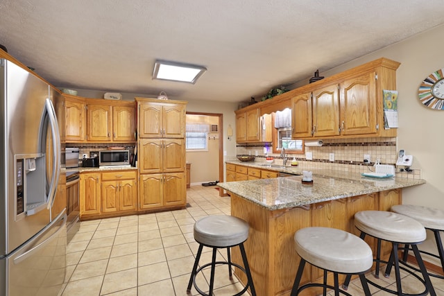 kitchen with a breakfast bar area, appliances with stainless steel finishes, kitchen peninsula, sink, and light stone counters