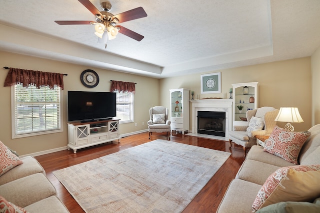 living room featuring a raised ceiling, a textured ceiling, hardwood / wood-style floors, and ceiling fan