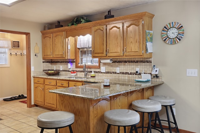 kitchen featuring kitchen peninsula, sink, light stone countertops, and a breakfast bar