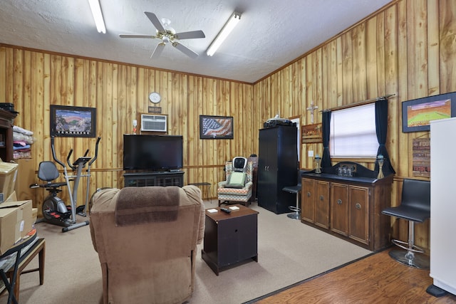 living room featuring hardwood / wood-style flooring, wood walls, ceiling fan, ornamental molding, and a textured ceiling