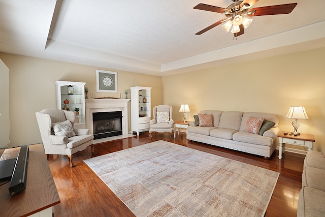 living room featuring a raised ceiling, ceiling fan, dark hardwood / wood-style flooring, and a fireplace