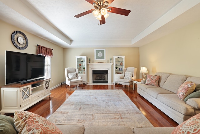 living room featuring a tray ceiling, ceiling fan, and dark hardwood / wood-style flooring