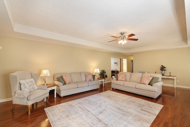 living room featuring ceiling fan, dark hardwood / wood-style floors, and a raised ceiling