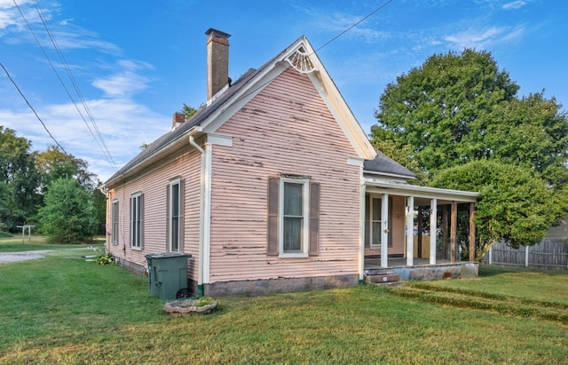 view of property exterior featuring a porch, a lawn, a chimney, and fence