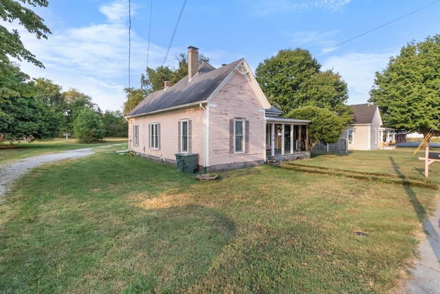 view of side of property featuring a chimney, a porch, and a lawn