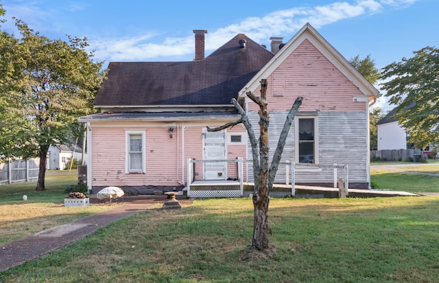 rear view of house featuring roof with shingles, a lawn, and a chimney