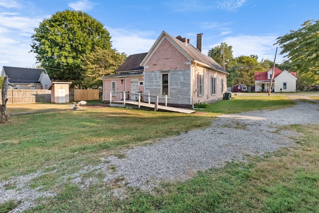 back of house with a lawn, a chimney, an outbuilding, a storage unit, and fence