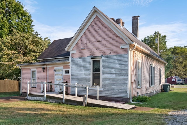 rear view of property with a lawn, a chimney, and fence