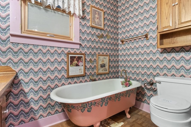 bathroom with baseboards, a freestanding bath, toilet, and wallpapered walls