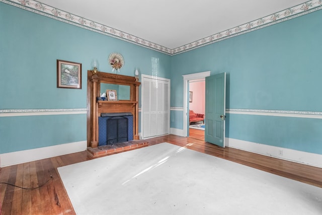 unfurnished living room with a brick fireplace, baseboards, and wood finished floors