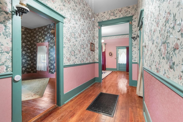 hallway with a wainscoted wall, visible vents, hardwood / wood-style floors, baseboards, and wallpapered walls