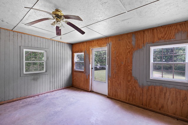 spare room with ceiling fan, wooden walls, concrete floors, and plenty of natural light