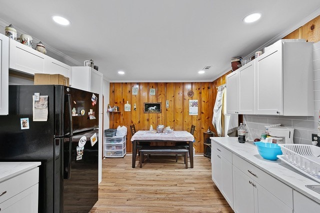 kitchen with black refrigerator, light hardwood / wood-style flooring, light stone counters, and white cabinetry