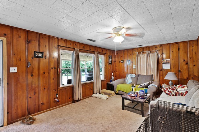 living room with wood walls, ceiling fan, and carpet flooring