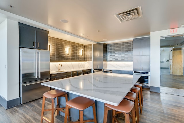 kitchen featuring appliances with stainless steel finishes, light stone countertops, a center island with sink, and decorative backsplash