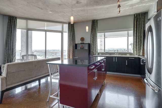 kitchen featuring a kitchen island, stainless steel fridge, hanging light fixtures, sink, and expansive windows