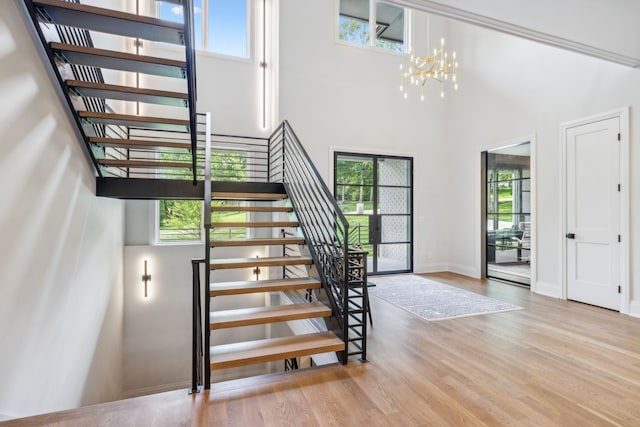 stairs featuring a towering ceiling, wood-type flooring, and a notable chandelier