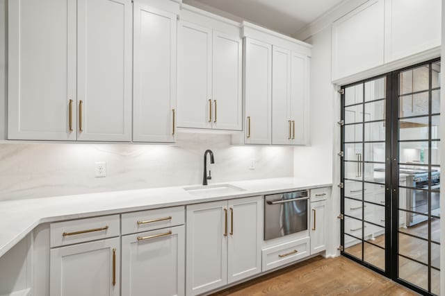 kitchen featuring light hardwood / wood-style floors, ornamental molding, sink, decorative backsplash, and white cabinets