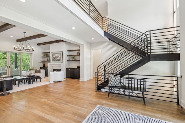 stairs with a towering ceiling, hardwood / wood-style floors, beam ceiling, and a notable chandelier