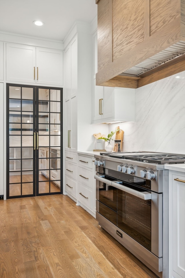 kitchen with white cabinetry, custom range hood, stainless steel stove, and light hardwood / wood-style floors